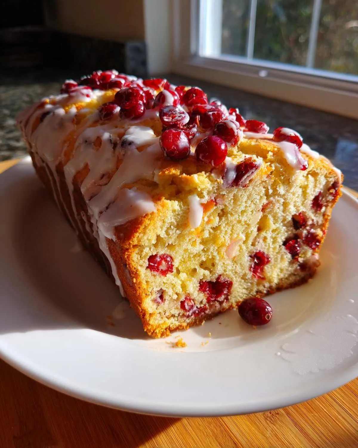 A freshly baked loaf of cranberry orange bread, drizzled with white glaze and topped with whole cranberries.