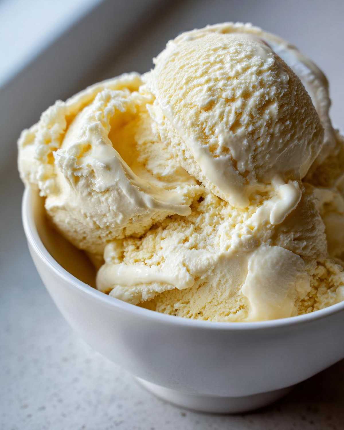 Close-up of creamy scoops of homemade banana ice cream melting slightly in a white bowl.