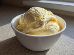 Close-up of creamy scoops of homemade banana ice cream served in a white bowl, highlighted by sunlight.