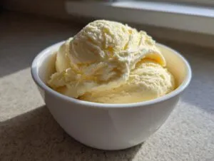Close-up of creamy scoops of homemade banana ice cream served in a white bowl, highlighted by sunlight.