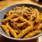 Close-up of creamy beef pasta made with penne noodles coated in a rich, orange sauce with ground beef.