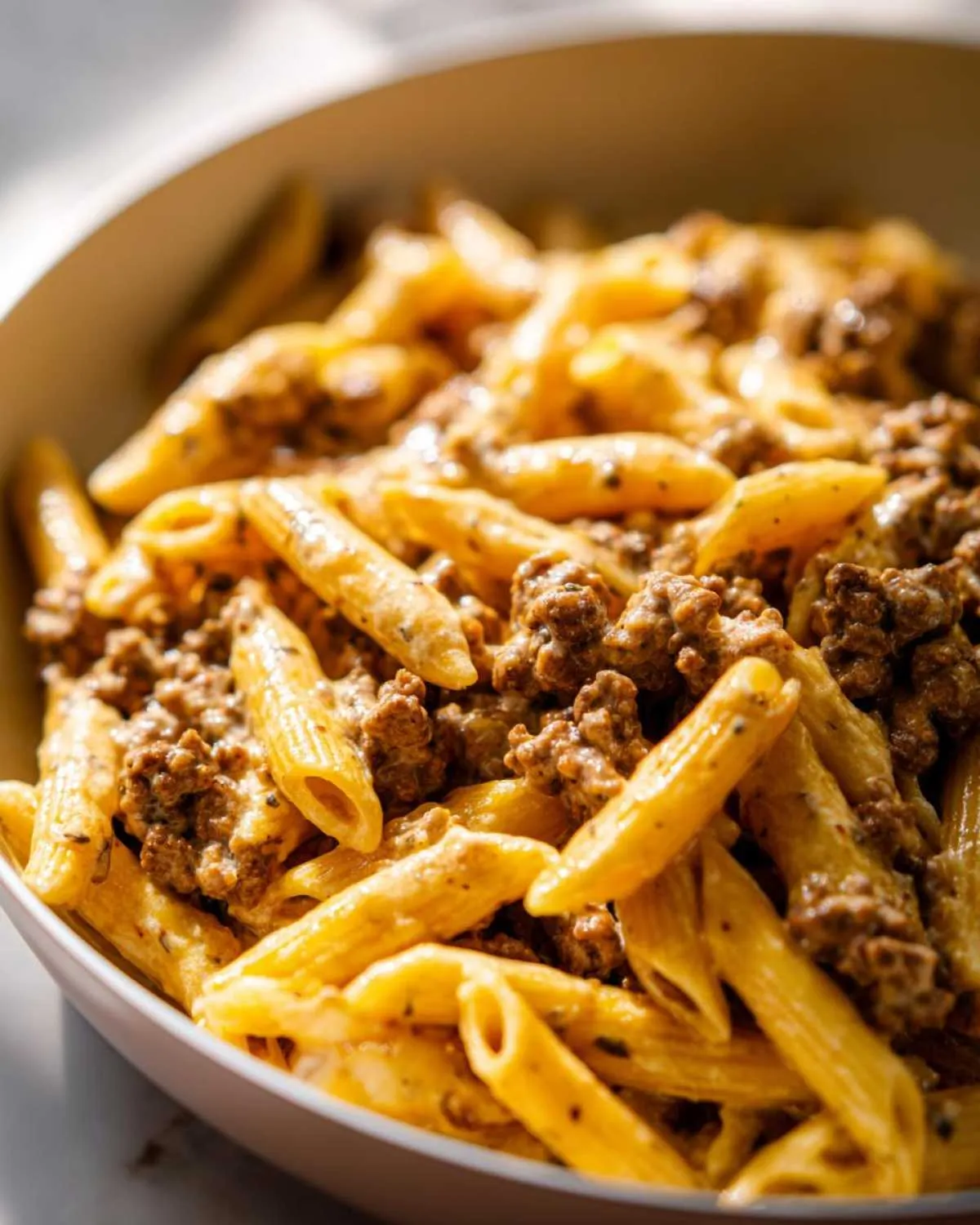 Close-up of creamy penne pasta mixed generously with seasoned ground beef, a perfect example of beef pasta.