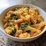 A close-up of creamy, cheesy broccoli pasta made with rotini noodles, served in a white bowl.