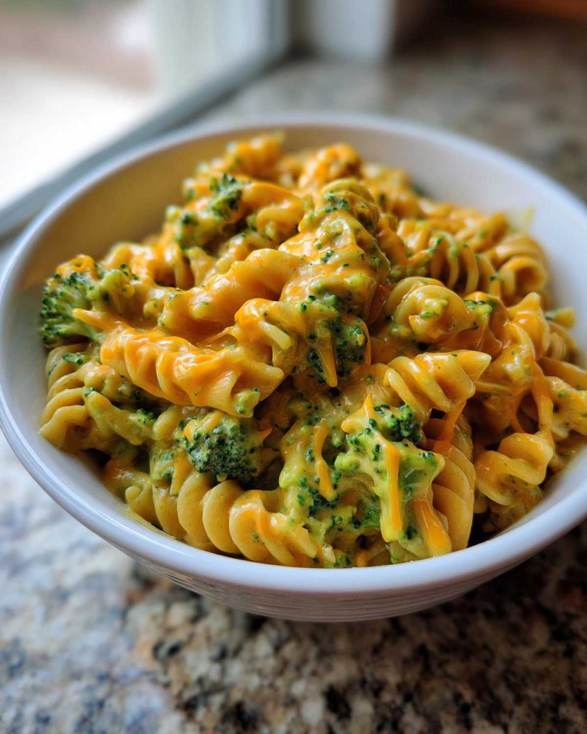 Close-up of creamy, cheesy broccoli pasta made with rotini noodles in a white bowl.