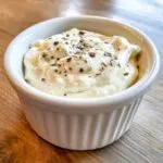 Close-up of creamy horseradish sauce for prime rib, topped with dried herbs and pepper, served in a white ramekin.