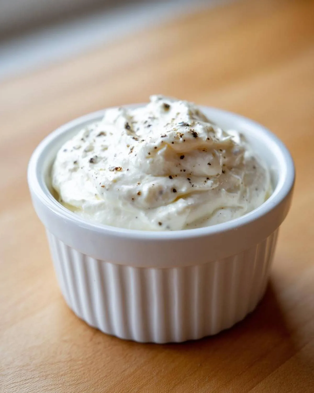 A small white ramekin filled with creamy horseradish sauce for prime rib, topped with black pepper.
