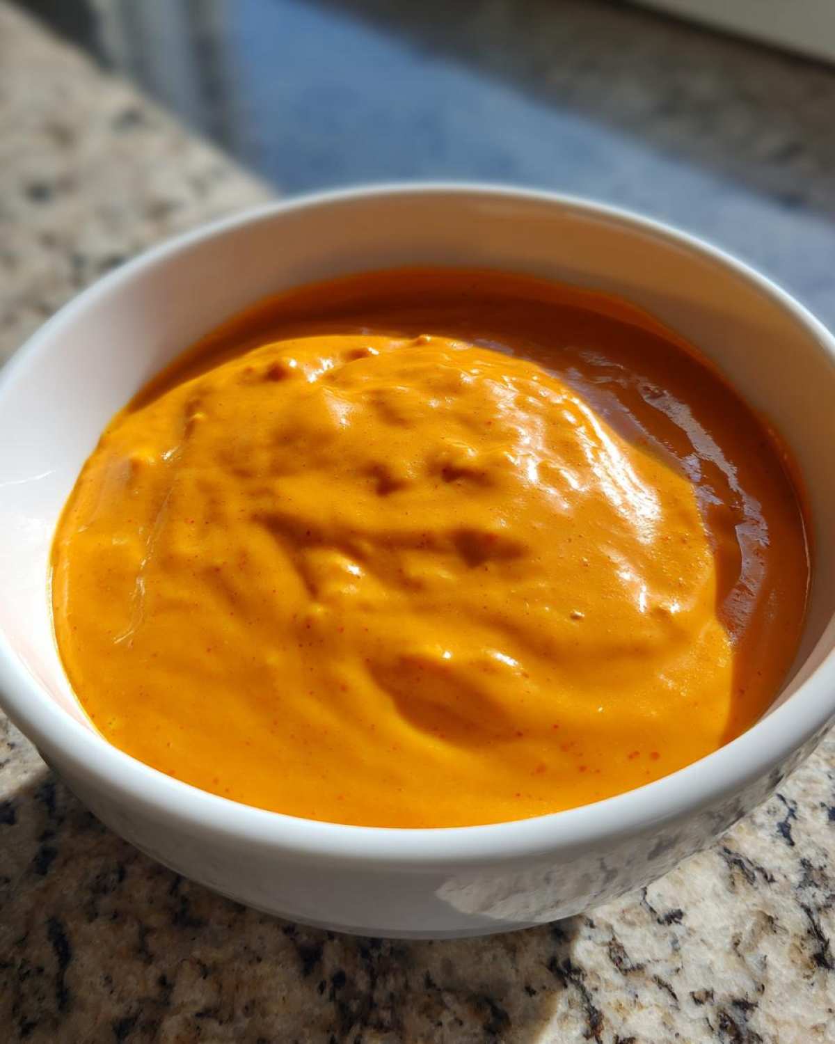 Close-up of vibrant, creamy orange nacho cheese sauce filling a small white bowl.