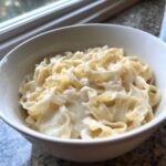 A white bowl filled with fettuccine pasta generously coated in creamy olive garden alfredo sauce.