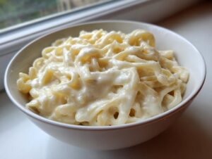 A white bowl filled with fettuccine pasta generously coated in rich, creamy olive garden alfredo sauce.