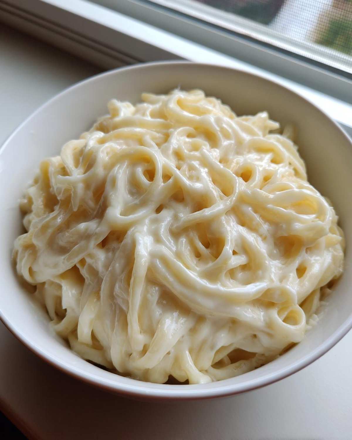A white bowl filled with fettuccine pasta generously coated in creamy olive garden alfredo sauce.
