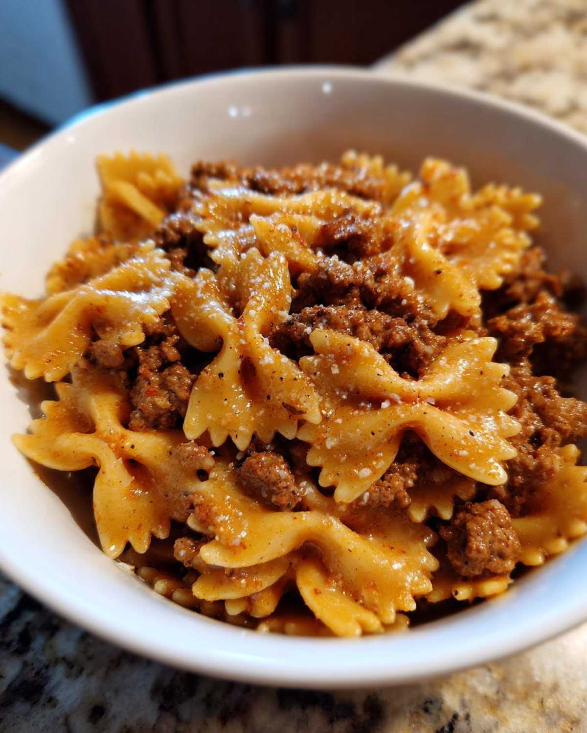 Close-up of creamy parmesan garlic beef bowtie pasta served in a white bowl, topped with grated cheese.