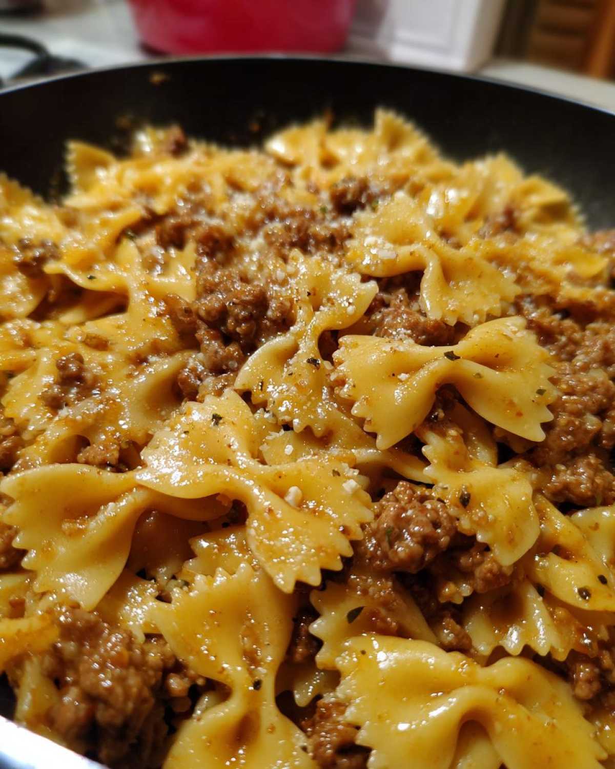 Close-up of creamy parmesan garlic beef bowtie pasta mixed together in a dark skillet, topped with grated cheese.
