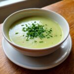 A creamy bowl of vibrant potato leek soup garnished generously with freshly chopped chives.