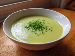 A close-up of creamy potato leek soup in a white bowl, topped with fresh chopped chives.