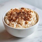 A close-up of creamy rice pudding recipe served in a white bowl, generously dusted with ground cinnamon.