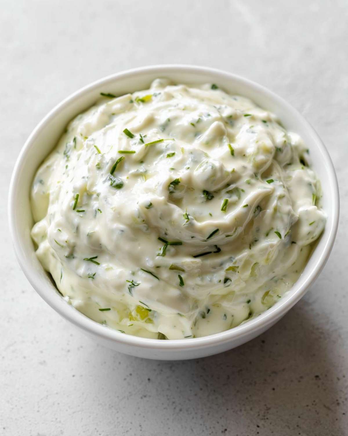 Close-up of creamy, chunky tartar sauce mixed with fresh green herbs in a white bowl.