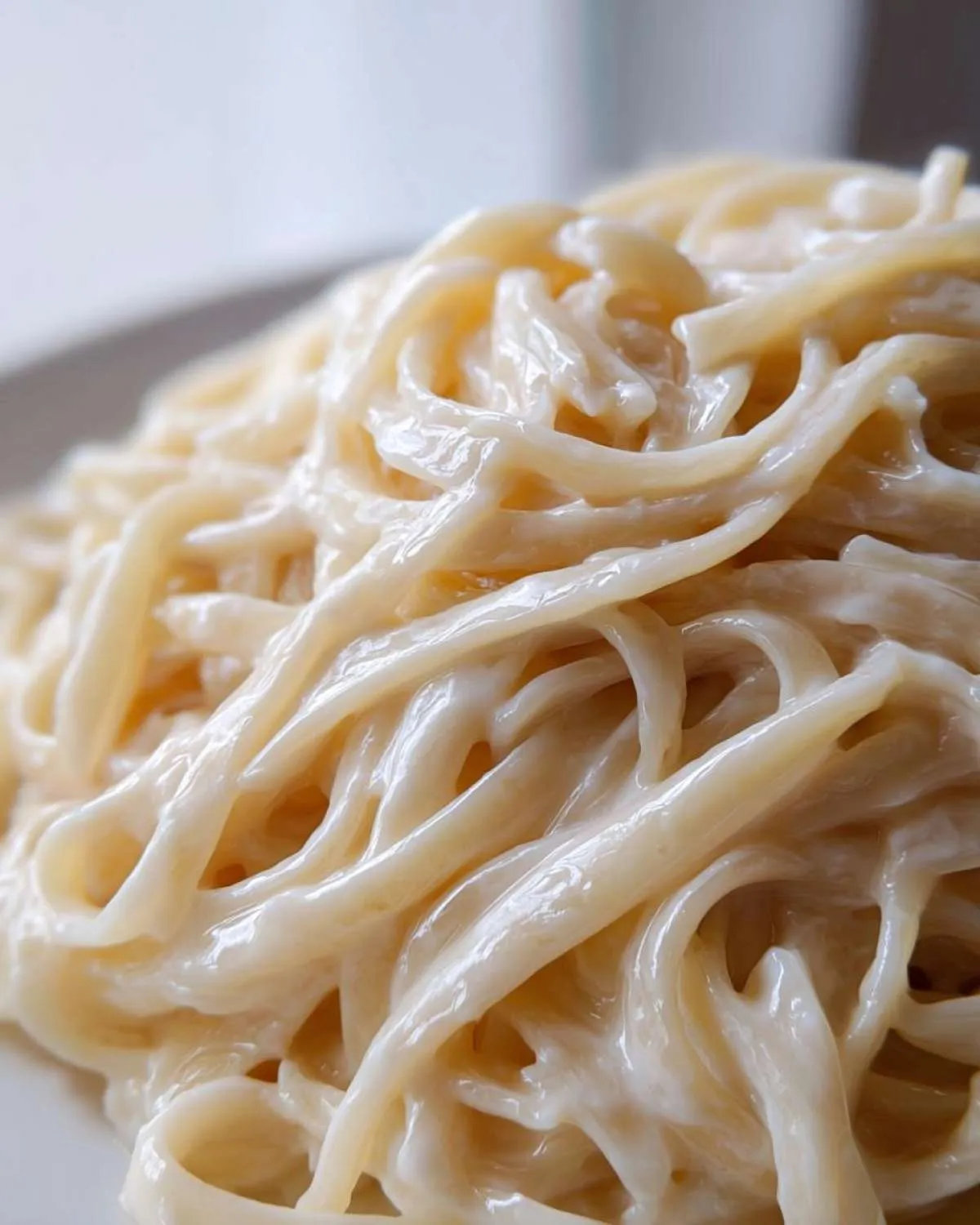 Extreme close-up of fettuccine noodles coated thickly in creamy vegan alfredo sauce.
