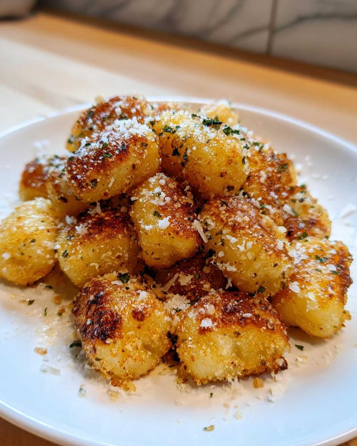 A plate piled high with crispy, golden brown air fryer gnocchi topped with grated Parmesan cheese and chopped parsley.
