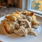 A close-up of a serving of crock pot chicken and stuffing topped with creamy gravy on a white plate.