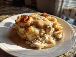 A hearty serving of crock pot chicken and stuffing topped generously with creamy brown gravy on a white plate.