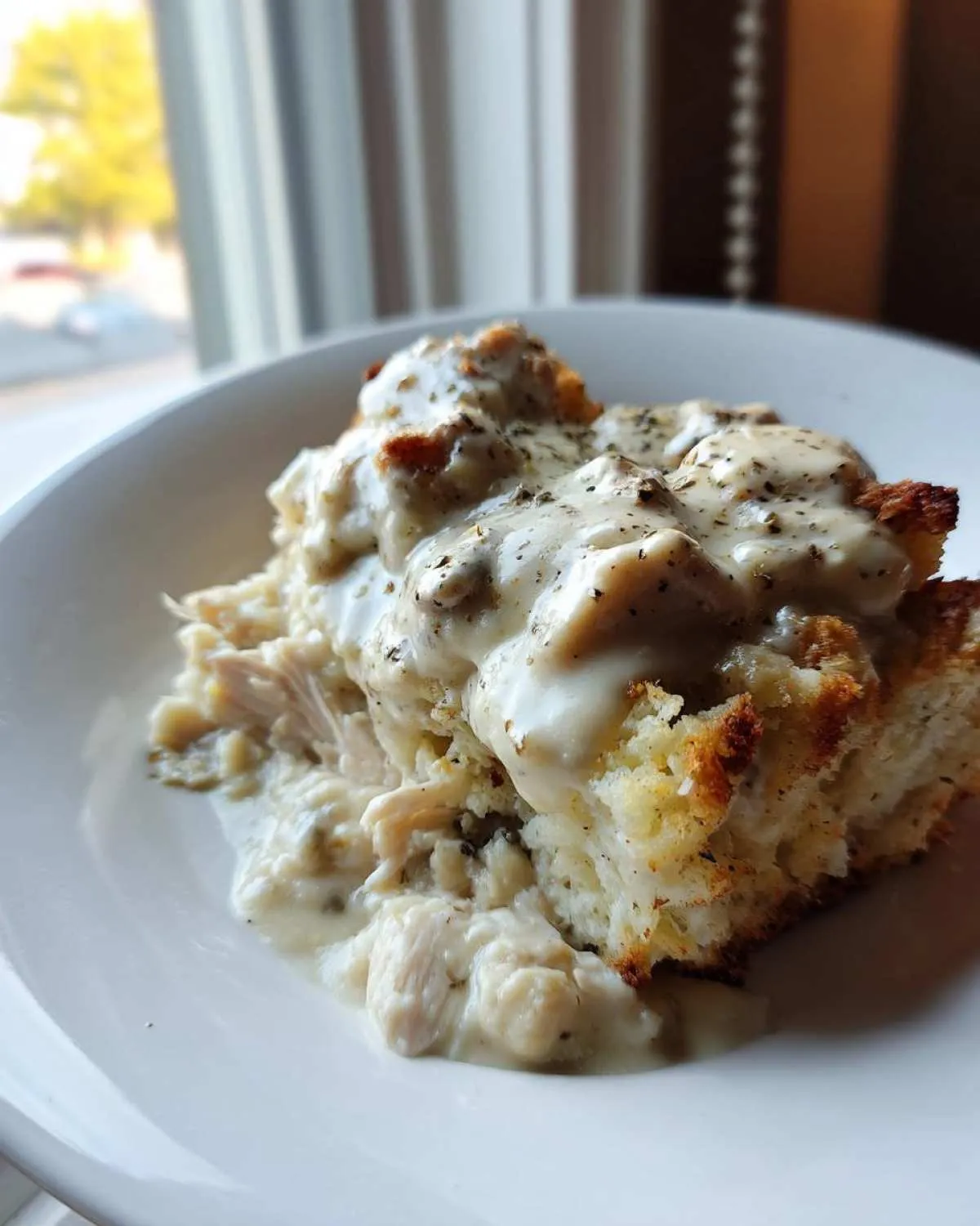 A close-up of a serving of crock pot chicken and stuffing topped with creamy white gravy and herbs.