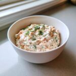 A close-up of creamy smoked salmon dip topped with fresh dill in a small white bowl.