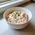 A close-up of creamy smoked salmon dip topped with fresh dill in a small white bowl.