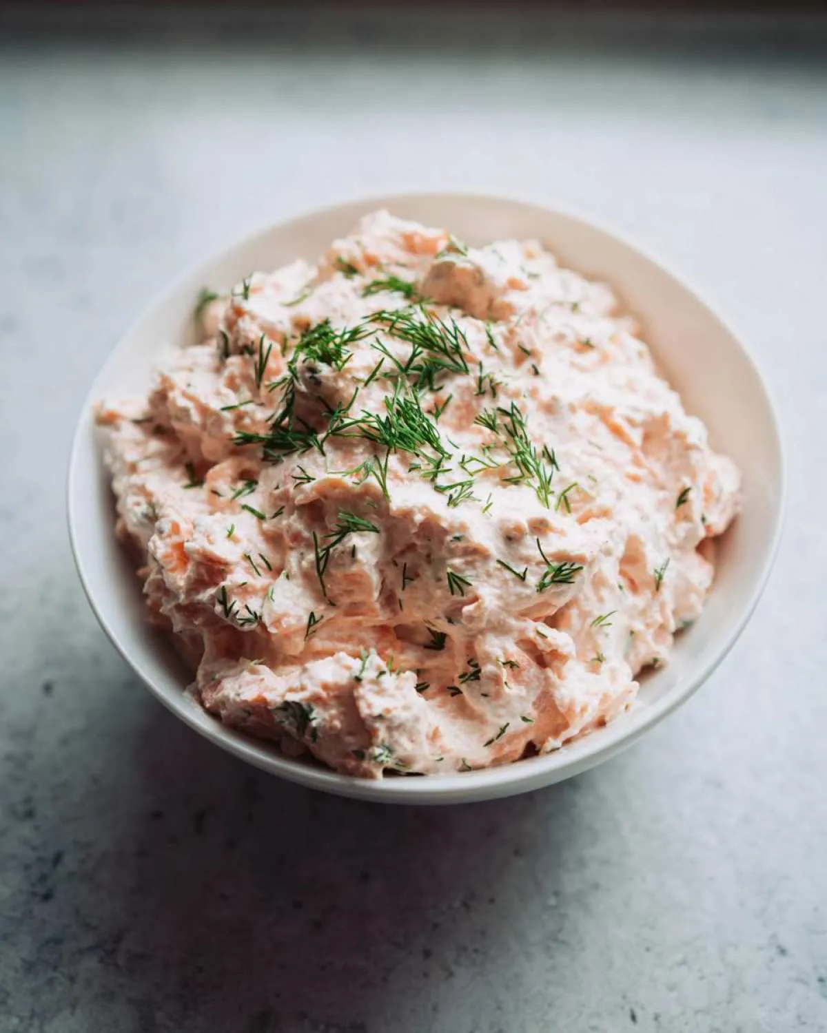 A close-up of creamy smoked salmon dip topped generously with fresh dill in a white bowl.