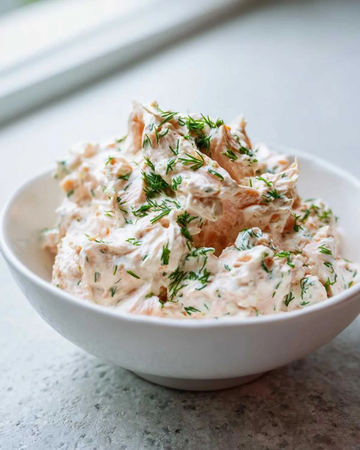 A white bowl filled with creamy smoked salmon dip, topped generously with fresh chopped dill.