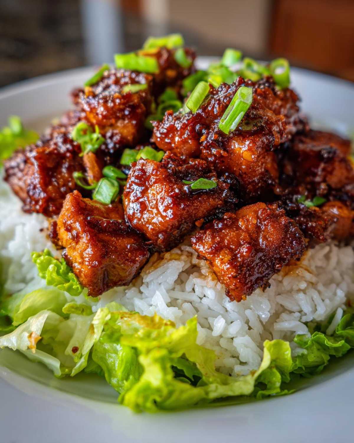 Close-up of glazed harissa chicken pieces served over white rice and fresh lettuce, topped with green onions.
