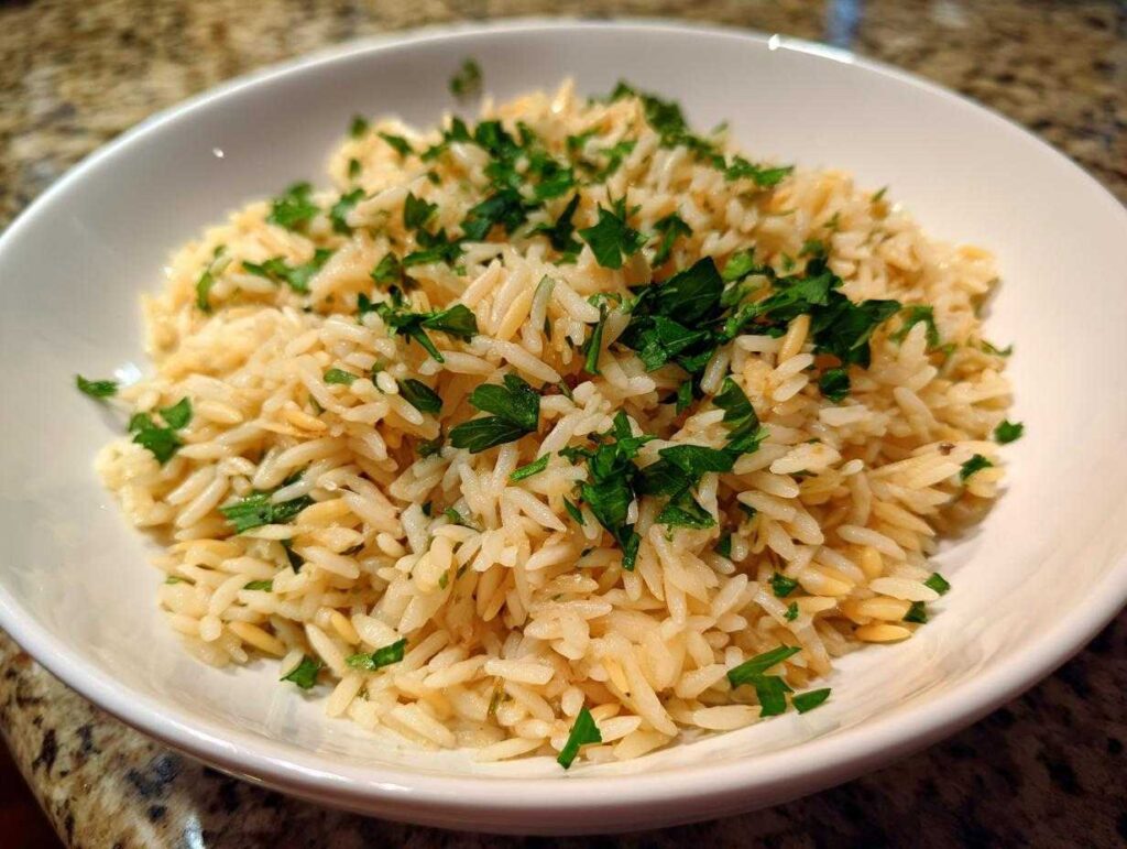 A close-up of fluffy rice pilaf served in a white bowl and garnished generously with chopped fresh parsley.