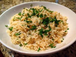 A close-up of fluffy rice pilaf served in a white bowl and garnished generously with chopped fresh parsley.