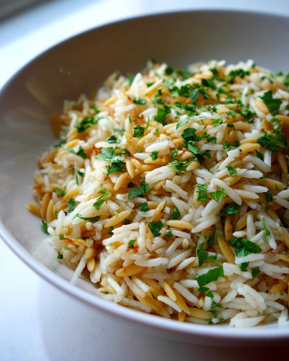 Close-up of fluffy rice pilaf mixed with toasted orzo pasta and topped with fresh chopped parsley.
