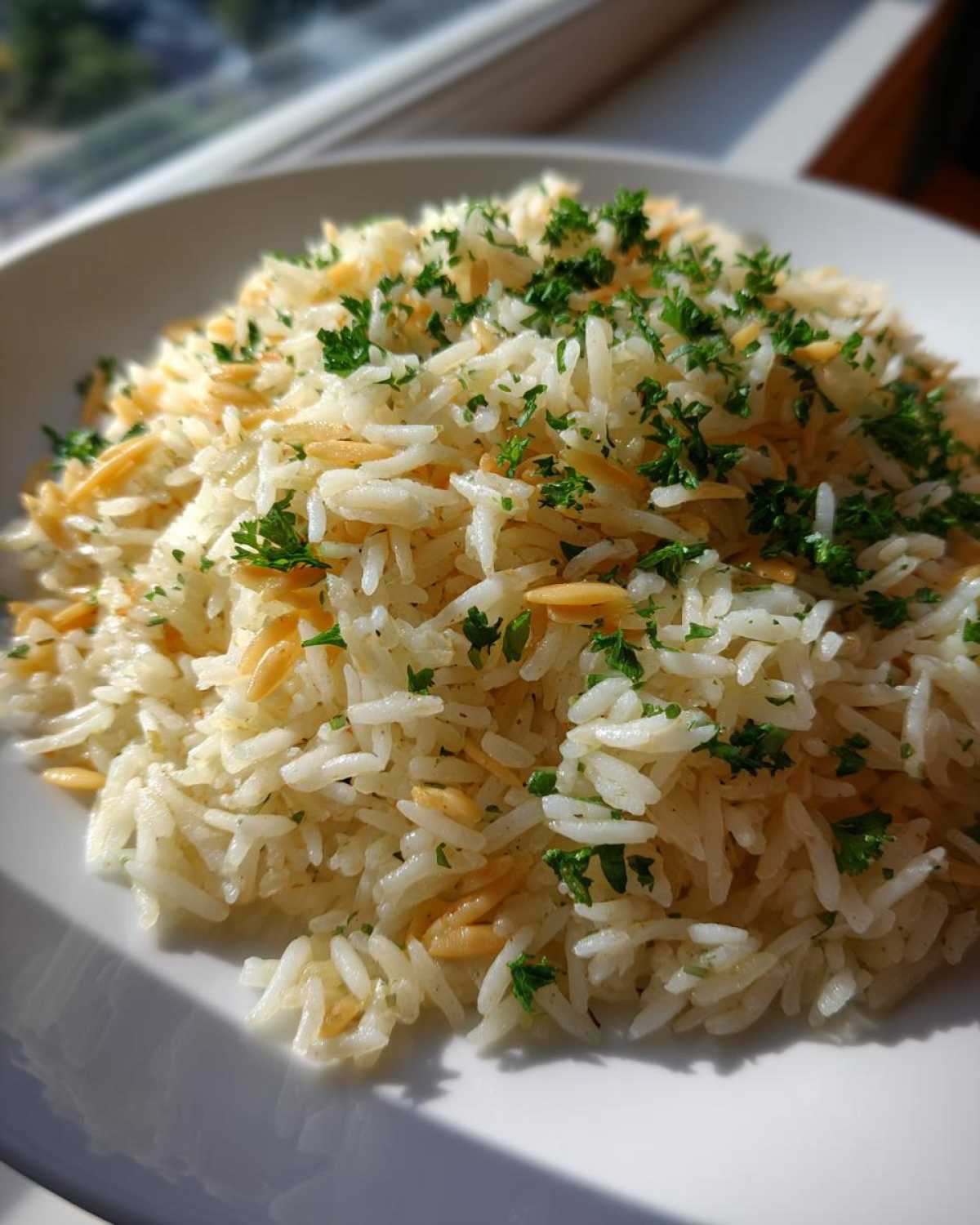A mound of fluffy rice pilaf mixed with toasted vermicelli and topped with fresh chopped parsley.