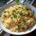 A white bowl filled with fluffy rice pilaf featuring toasted vermicelli and topped with fresh chopped parsley.