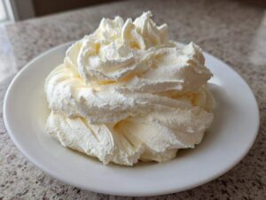 A generous swirl of fluffy, pale yellow vanilla buttercream frosting piped onto a small white plate.