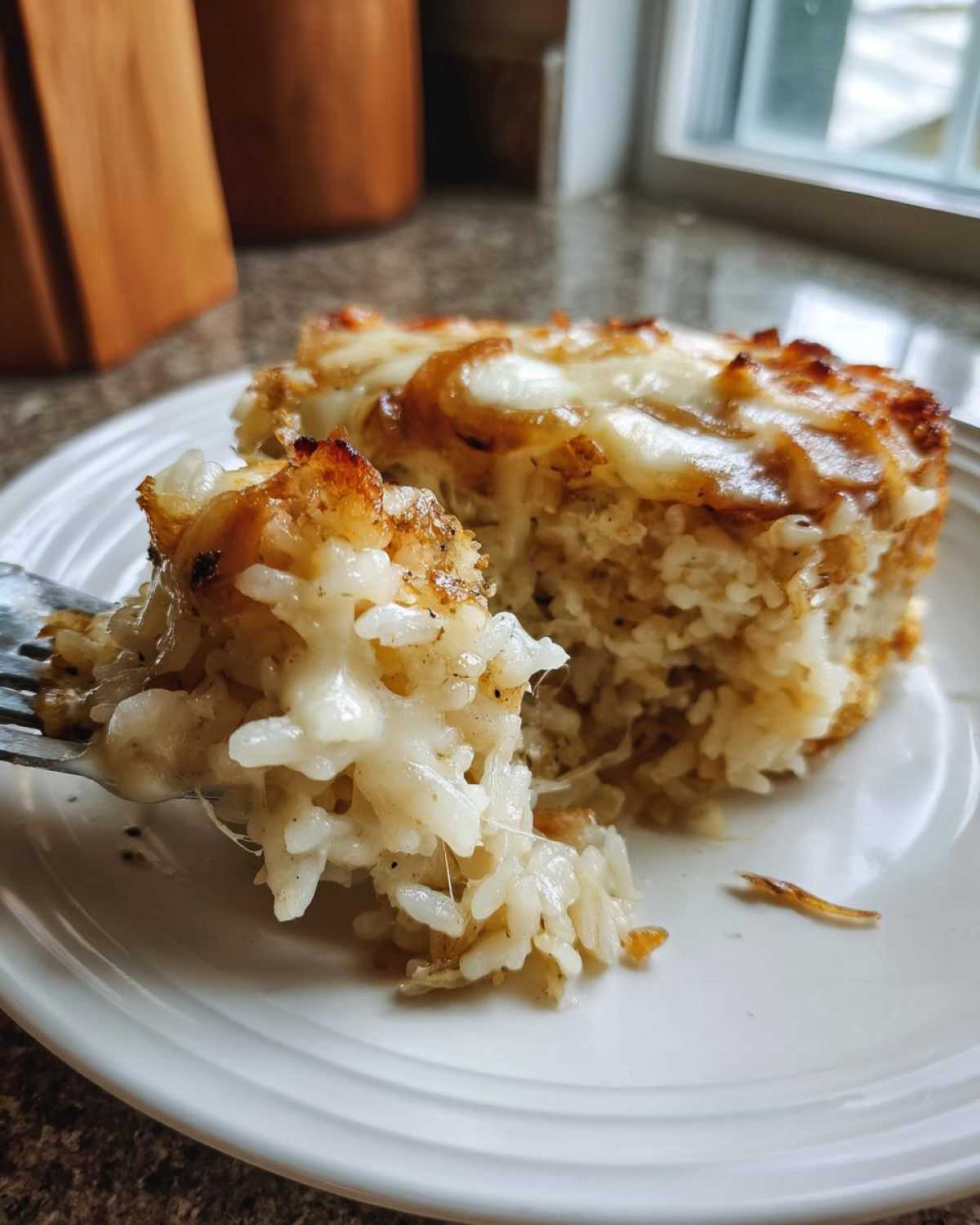 A fork pulls away a cheesy, gooey portion of french onion butter rice casserole from a larger serving.