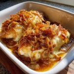 Close-up of baked french onion chicken topped with melted cheese and crispy fried onions in a white dish.