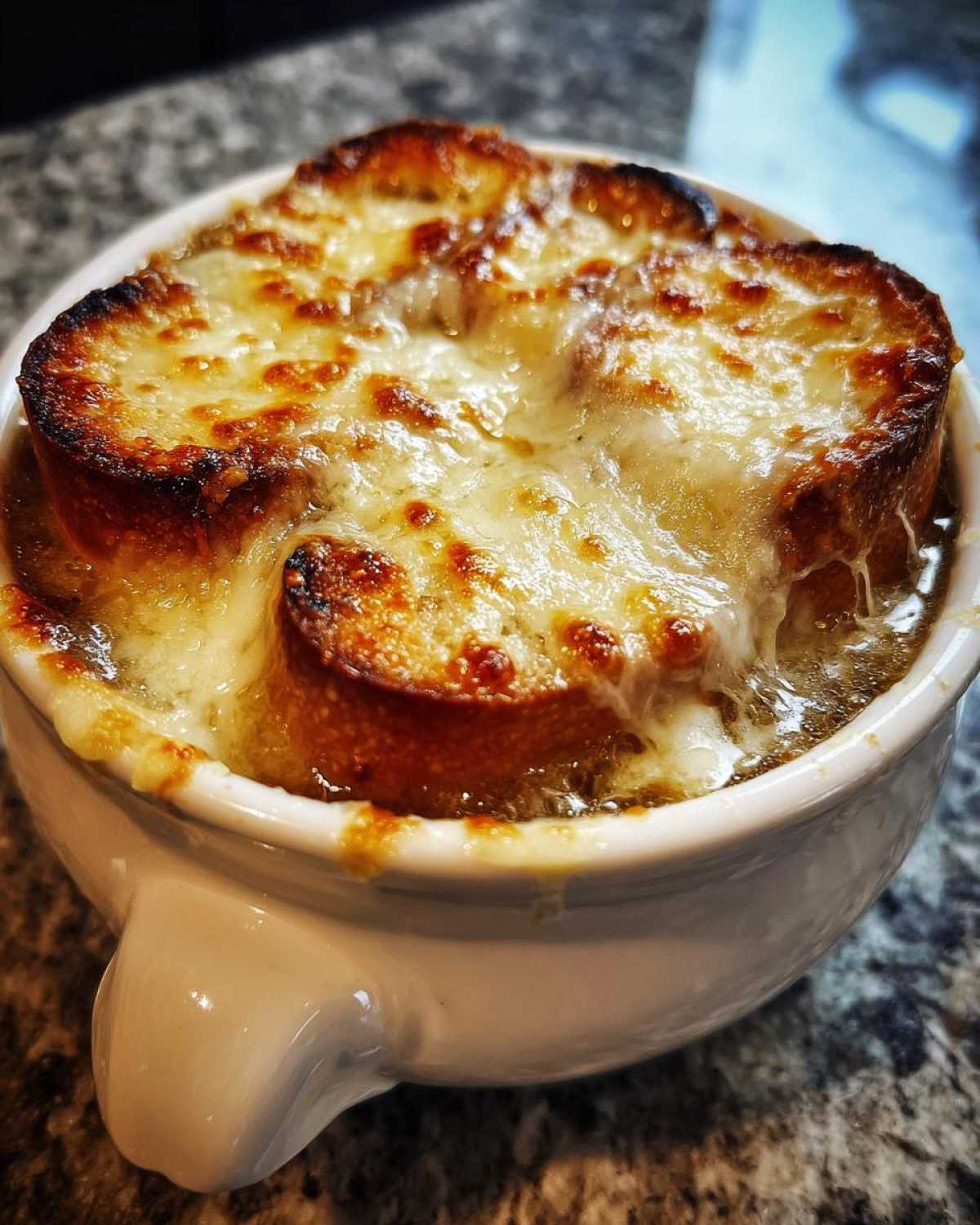 Close-up of a bowl of rich french onion soup topped with a thick layer of toasted bread and bubbly, melted Gruyère cheese.