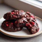 Close-up of fudgy chocolate cherry cookies, showing melted chocolate chips and bright red cherry pieces inside.