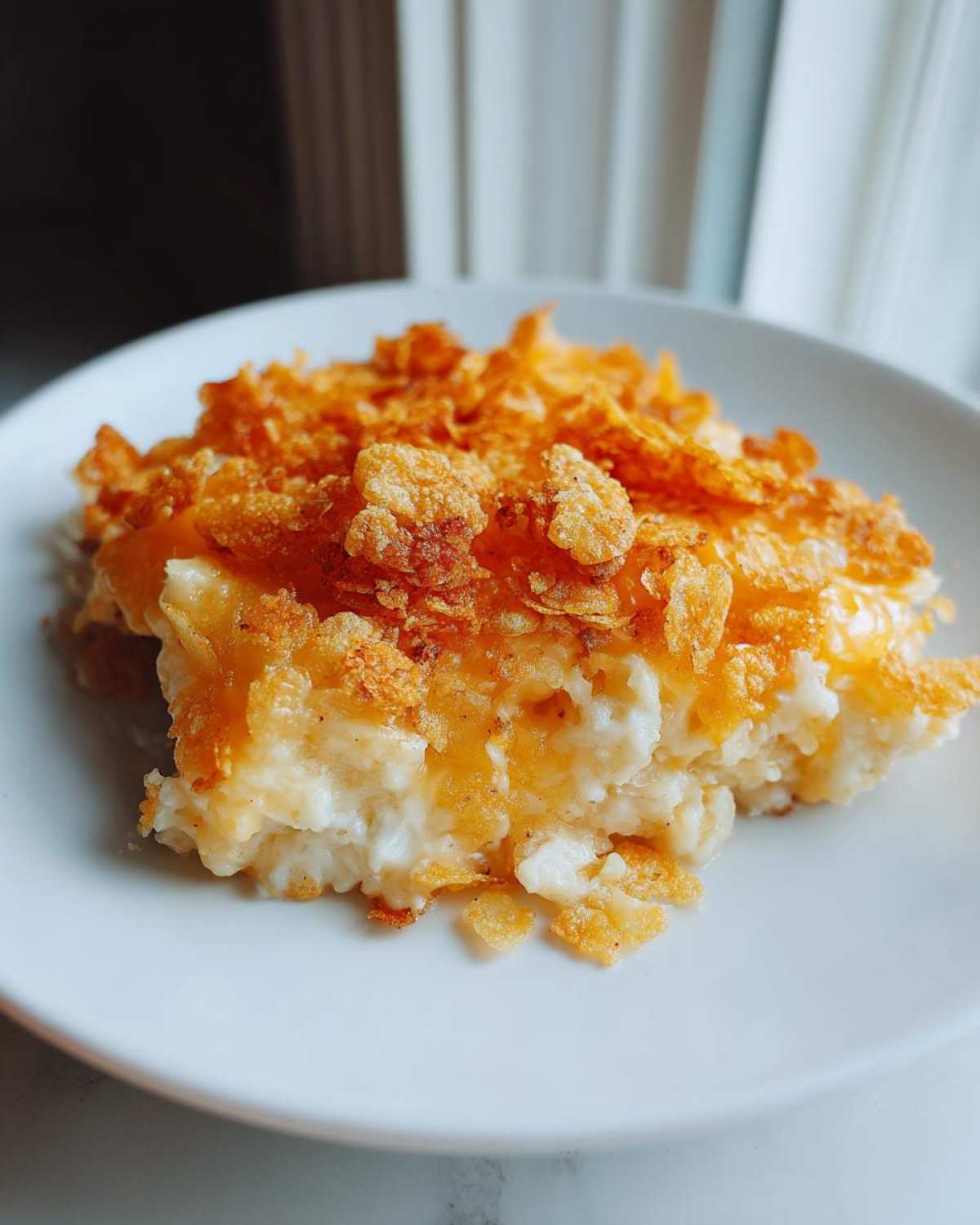 A close-up serving of creamy funeral potatoes recipe topped with golden, crunchy cornflakes.
