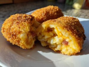 Close-up of golden brown, crispy potato croquettes, one is broken open revealing a cheesy potato and ham filling.