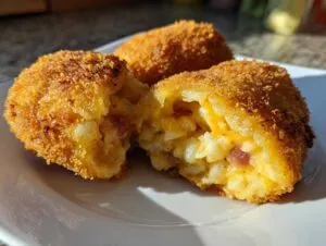 Close-up of golden brown, crispy potato croquettes, one is broken open revealing a cheesy potato and ham filling.