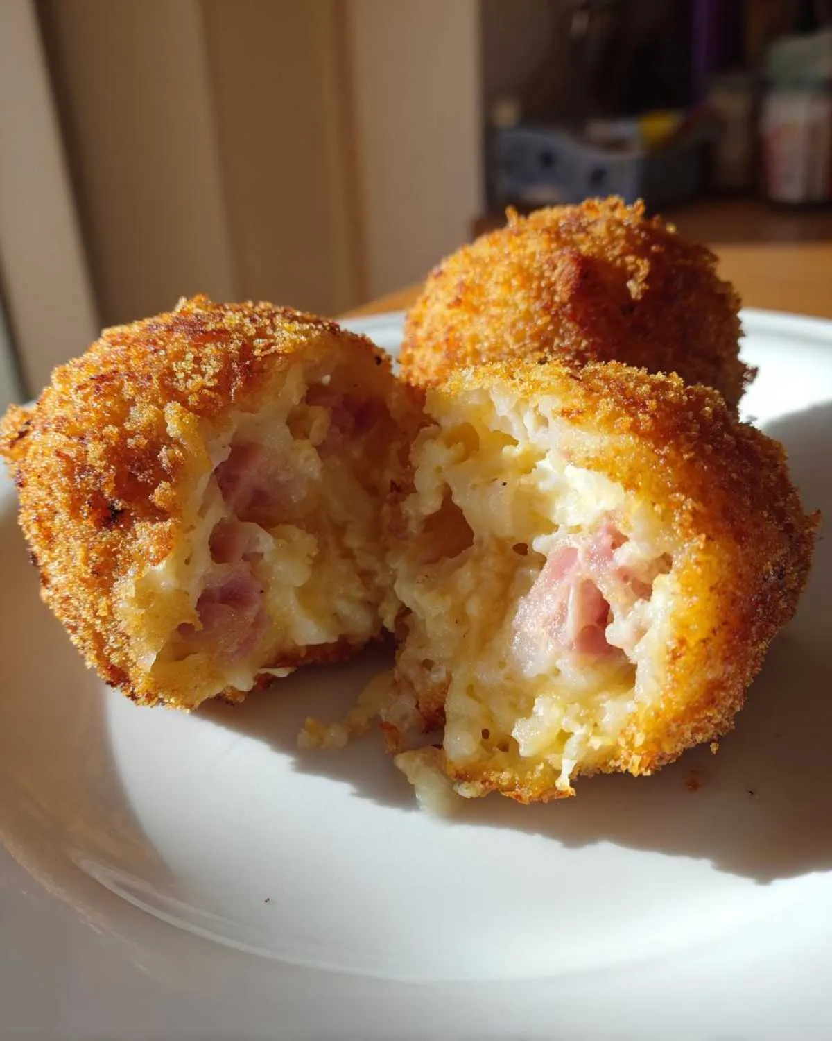 Close-up of golden brown potato croquettes, one cut in half revealing a creamy interior with pieces of ham.