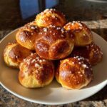 A stack of freshly baked, golden brown pretzel bites topped with coarse salt crystals.