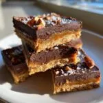 Close-up of stacked graham cracker toffee bars topped with chocolate, pecans, and flaky sea salt.