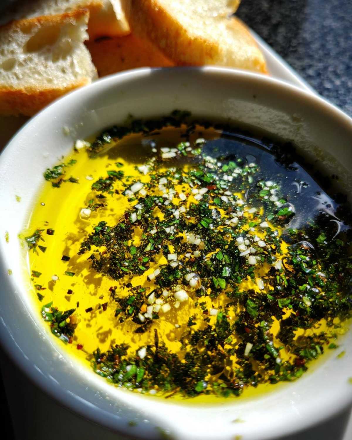 Close-up of bright yellow olive oil bread dip seasoned with chopped herbs and minced garlic.