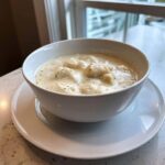 A white bowl filled with rich, creamy homemade cream of chicken soup featuring visible chunks of chicken and herbs.