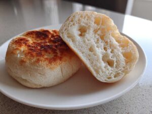 One whole and one halved homemade English muffin showing its signature nooks and crannies texture.