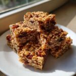 A stack of chewy homemade granola bars made with oats and dried cranberries, beautifully lit by sunlight.